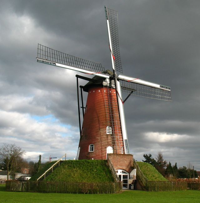 De Molen van Oelegem, een bakstenen beltmolen onder een donkere wolkenlucht.