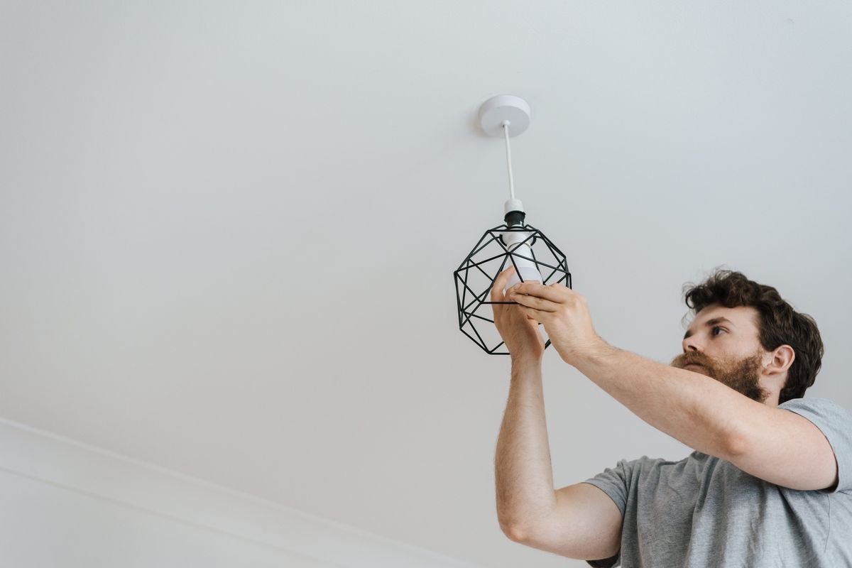 Een man hangt een zwarte draadlamp aan het plafond.