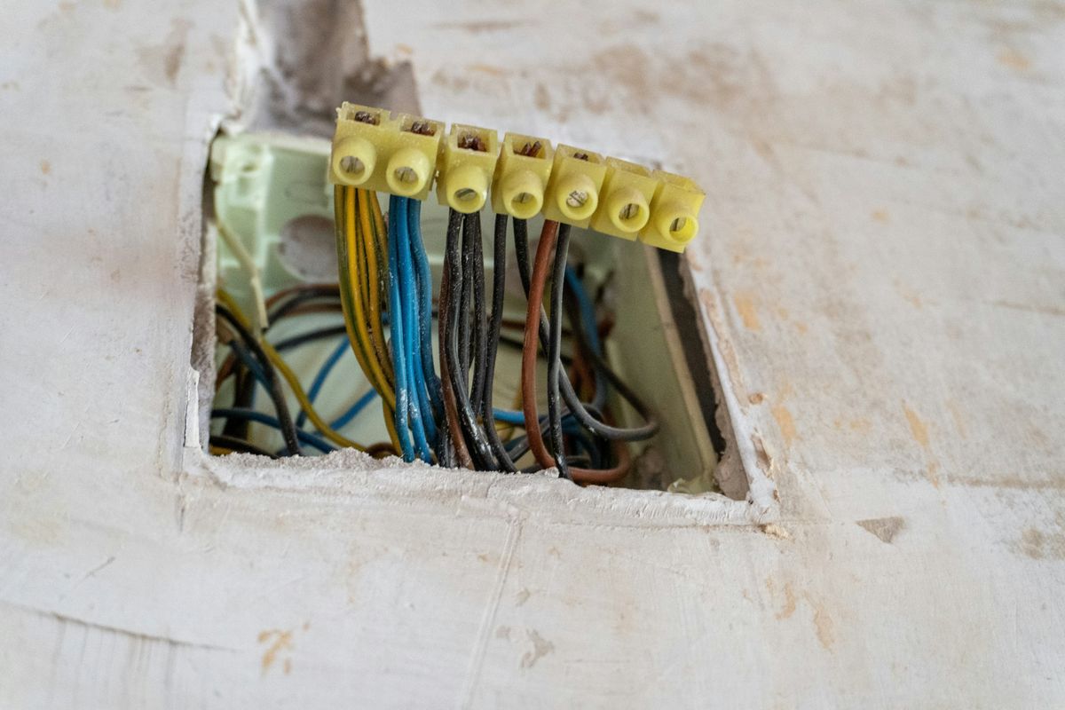 Een open aftakdoos in de muur met gekleurde draden in gele kroonsteentjes.